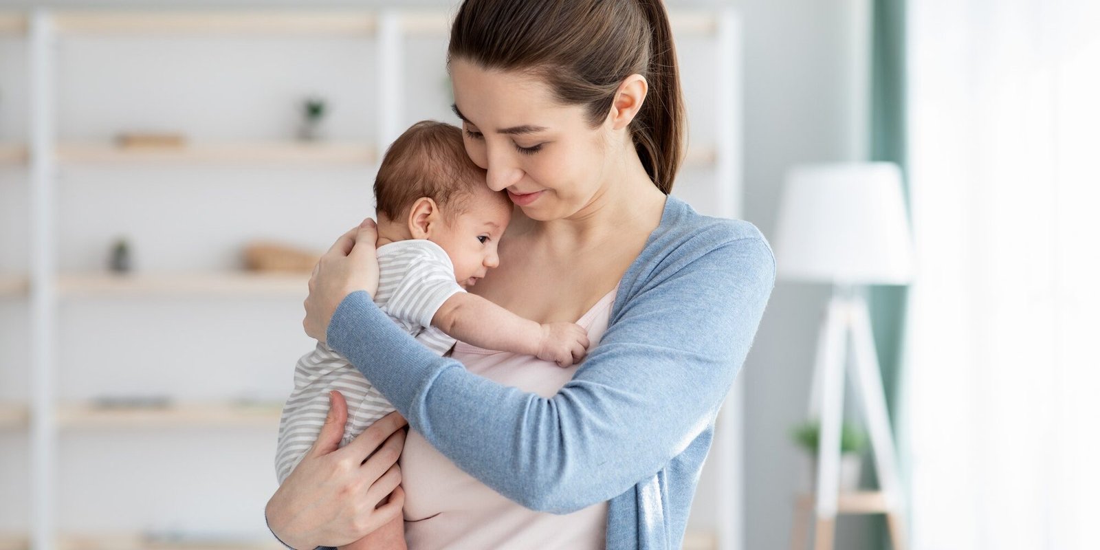 Young Smiling Mum Holding Her Adorable Newborn Baby, Tenderly Embracing Her Child