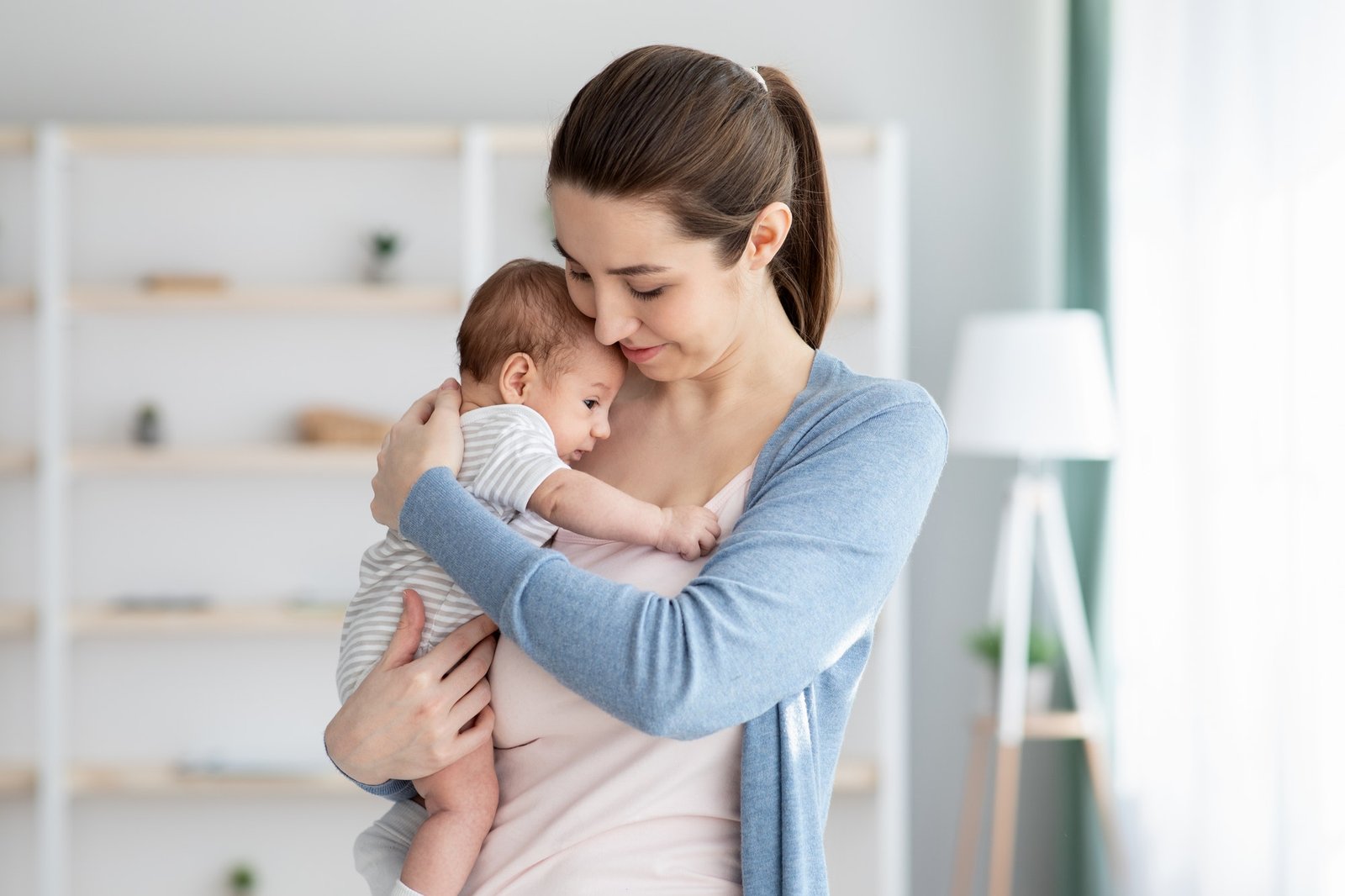 Young Smiling Mum Holding Her Adorable Newborn Baby, Tenderly Embracing Her Child Young Smiling Mum Holding Her Adorable Newborn Baby, Tenderly Embracing Her Child